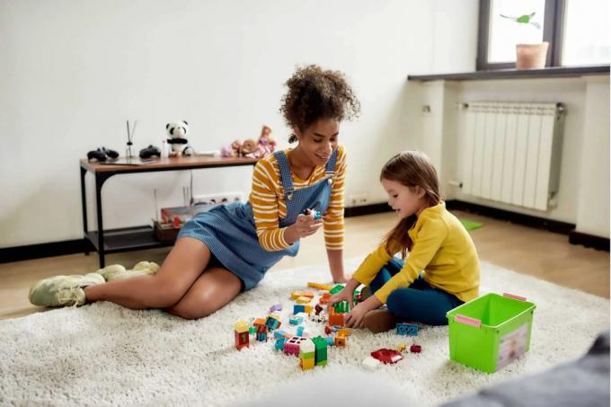 adolescente jugando lego con una niña sentada en el suelo. 